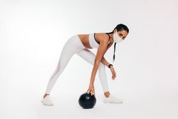 Woman in workout gear, and mask with medicine ball
