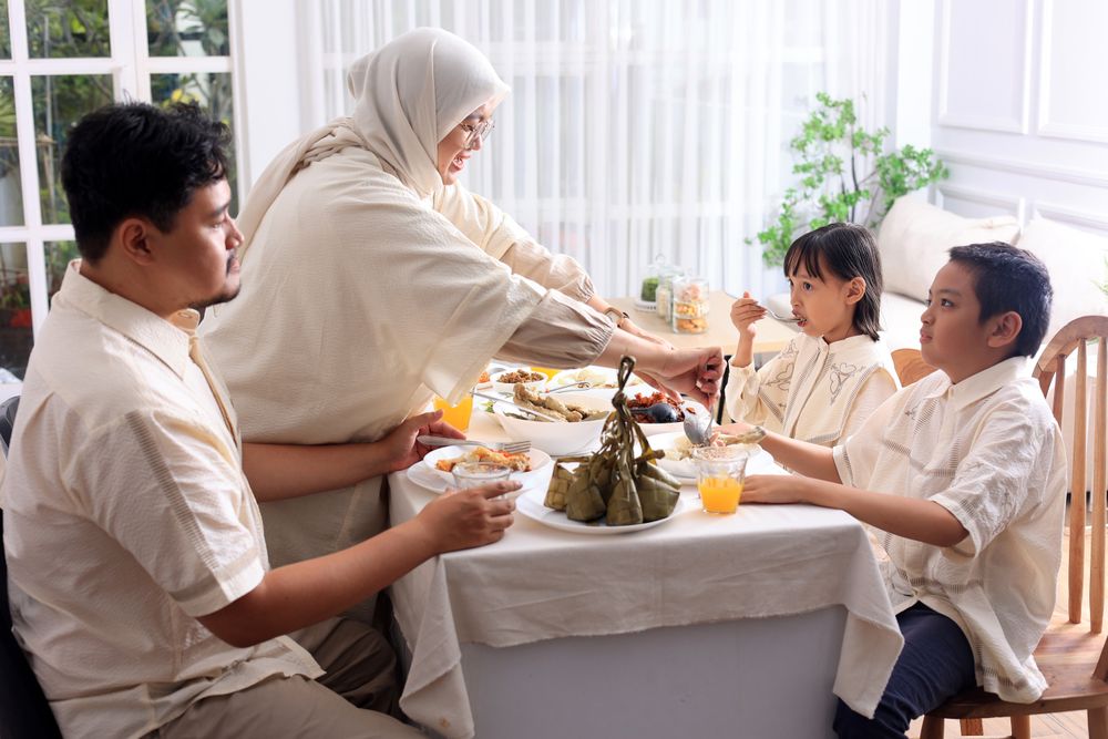 Muslim Woman Serving Foods to Her Husband and Kids in Dining Room While Having Dinner During Eid Mubarak at Home