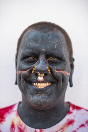 Man smiling with extreme body modification, full face tattoos and multiple gauge piercings