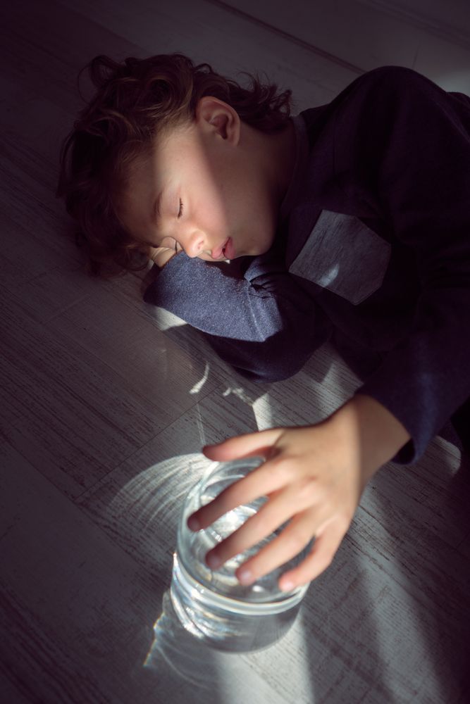 Little kid sleeping on floor with glass jar of water
