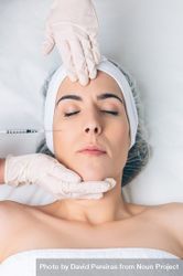 Aesthetician's hands in latex gloves injecting botox into female's cheek in a beauty salon 48BN2Y
