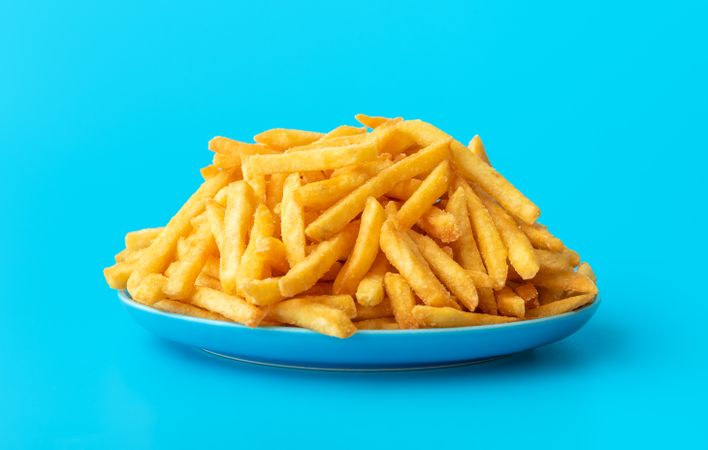 French fries on a plate isolated on a blue background