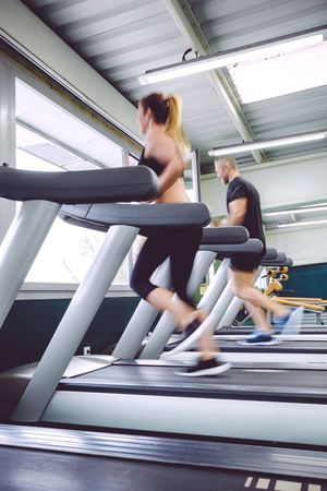 Side view of man and woman in motion on gym treadmills