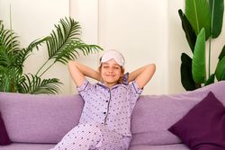 Relaxed girl in pajamas with sleep mask on couch.