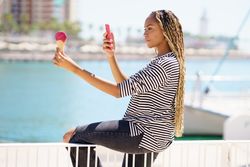 Female using smartphone to picture ice cream cone on the waterfront