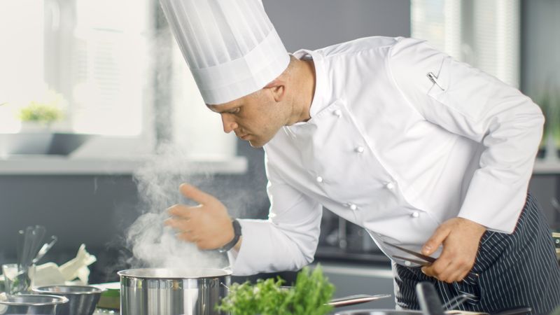 Famous Restaurant Chef Smells Steam From Saucepan. His Preparing Dishes in Modern Kitchen.