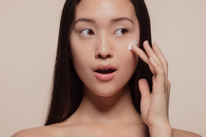 Woman applying moisturizer cream on her bare face
