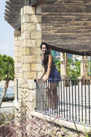 Beautiful hispanic woman in blue dress leaning over rail outside, vertical