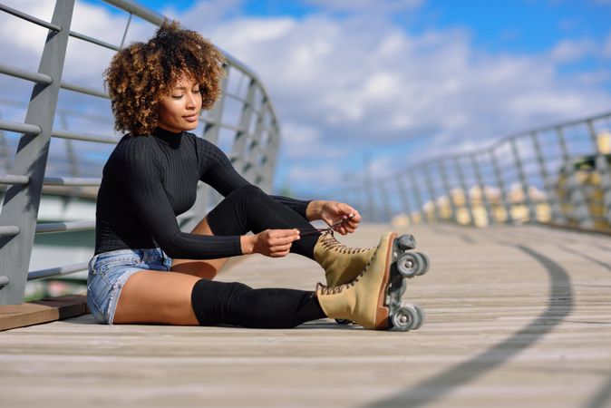 Woman with afro hairstyle putting on roller skates on wooden bridge