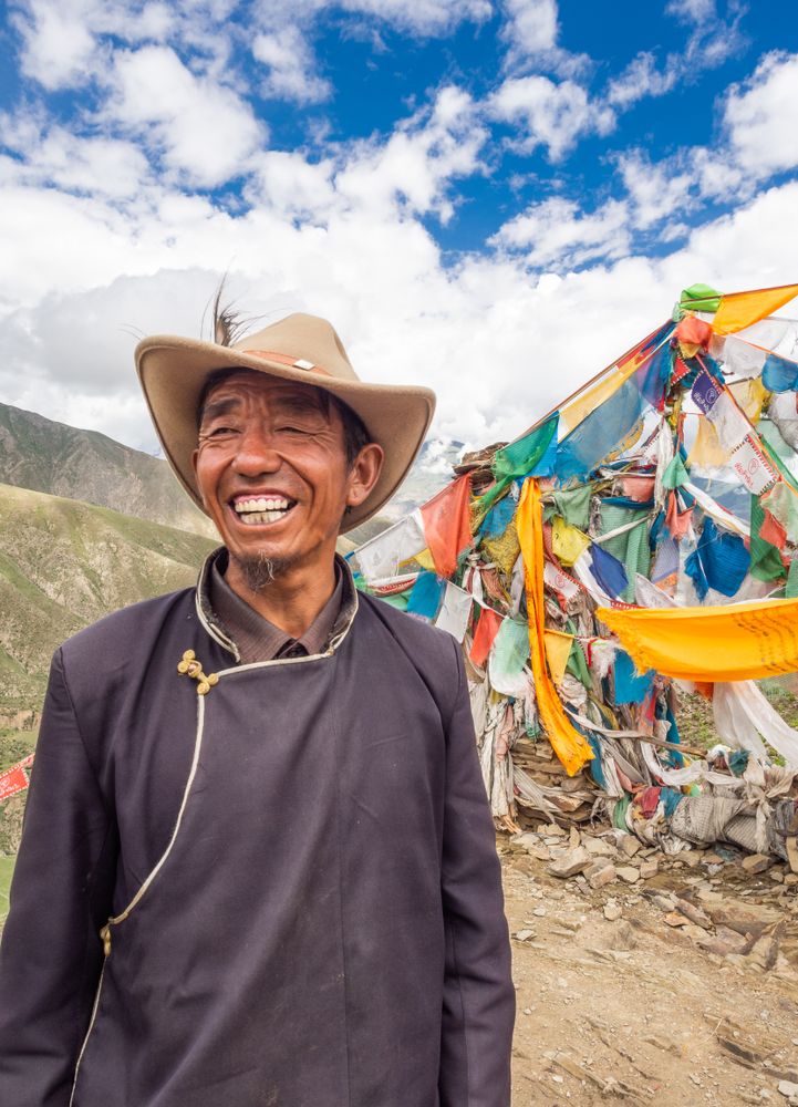 Tibet - August, 29 2014: Cheerful Tibetan man near flags composition