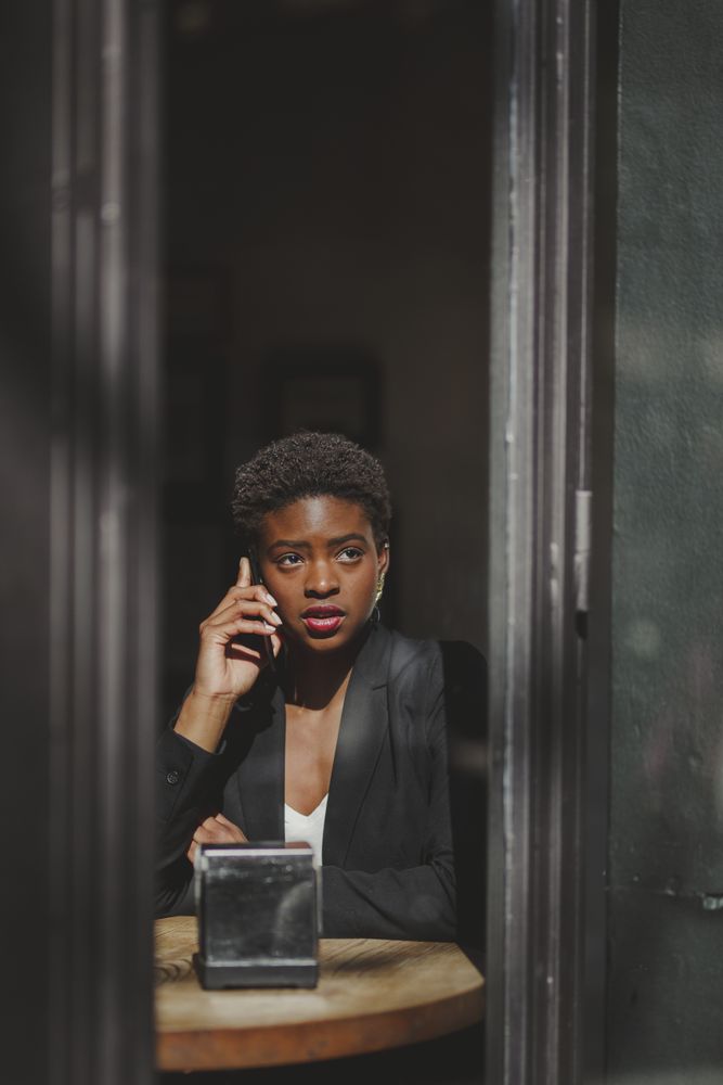 Serious stylish Black woman talking on smartphone in cafe