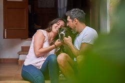 Happy couple playing with adorable dog on porch