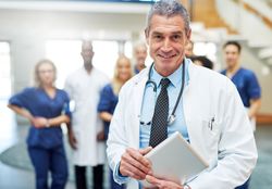 Smiling mature doctor in lab coat and stethoscope with his medical team in the background