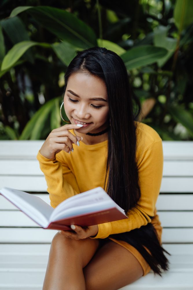 Graceful long haired Asian woman reading book on bench in park