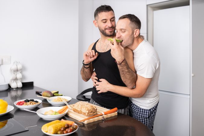 Cute male couple preparing food for lunch and tasing it as they go