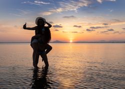 Woman carrying girlfriend on back and taking selfie in water at beach