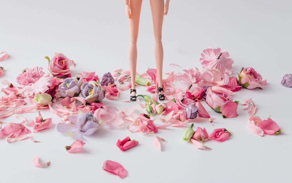 Doll standing with pink and violet flowers at feet