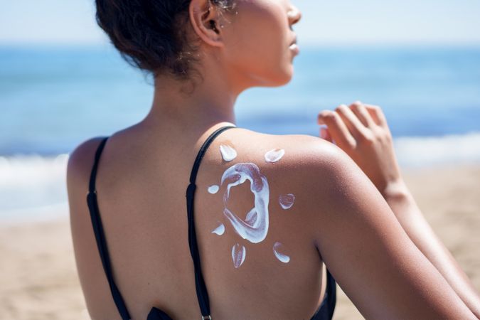 A woman joyfully applies sunscreen at the beach, savoring the ocean view on a sunny day