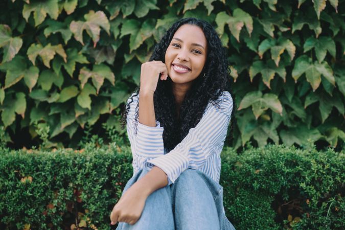 A Joyful Young Woman is Sitting in a Beautiful Garden Setting Surrounded by Lush Greenery