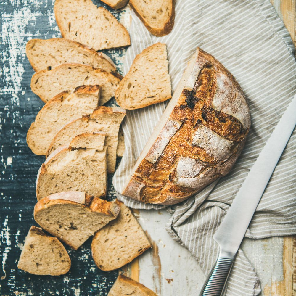 Homemade loaf of sliced bread with serrated knife, on wooden board and linen cloth