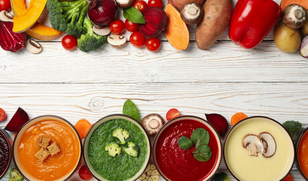 Line of soups and vegetables with copy space on wooden table