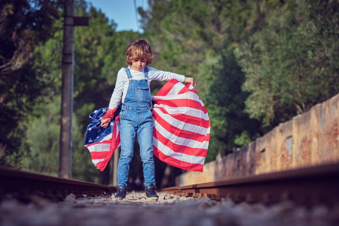 Preteen boy with waving American national flag standing on railr