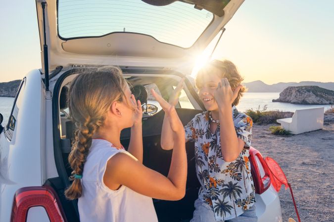 Cheerful children playing patty cake game near car on beach
