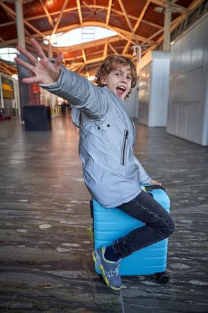 Cheerful kid sitting on suitcase