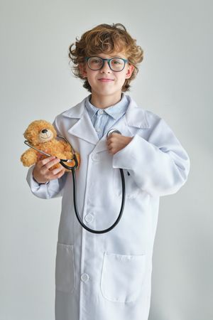 Smiling boy doctor with stethoscope and soft bear