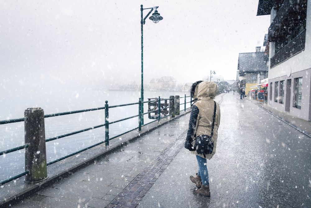 Woman walking near a lake during snowfall dressed in winter clothes
