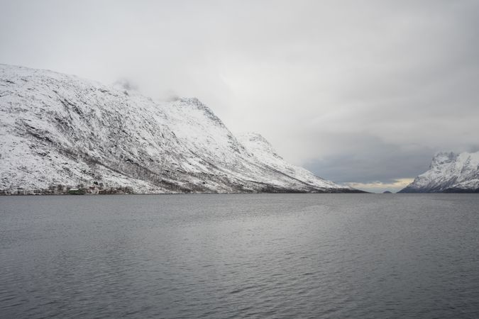 Tranquil lake against snowy hills in cold overcast weather