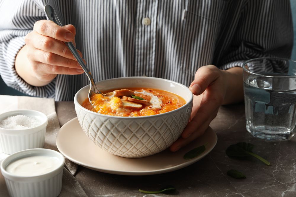Person dipping spoon in bowl of pumpkin soup on table