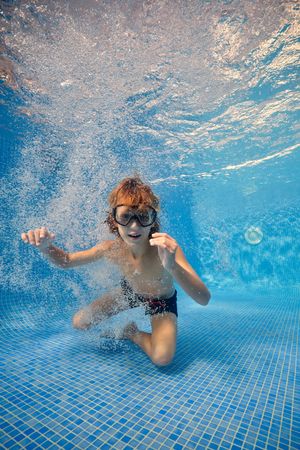 Boy in goggles swimming in blue clean water