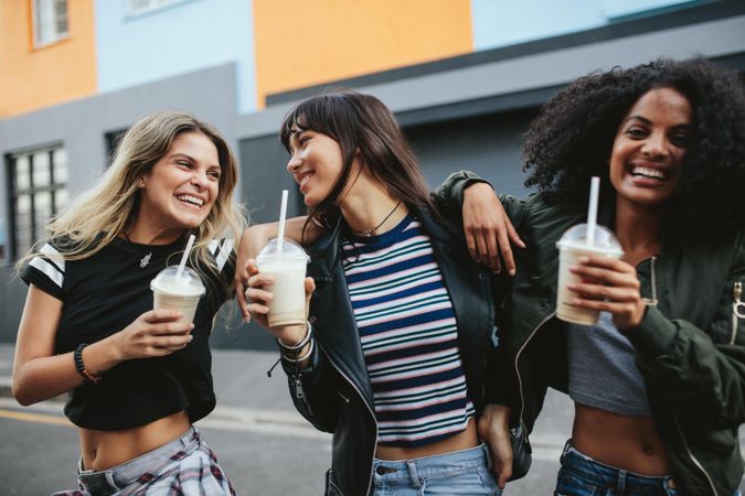 Happy group of females holding milkshakes while walking down street