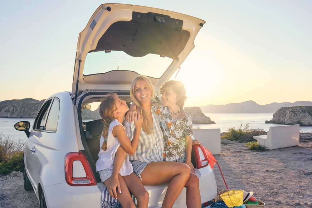 Smiling women with daughter and son sitting in car trunk