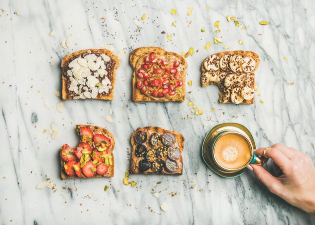 Toast topped with fresh fruit on marble background with hands holding coffee, horizontal composition