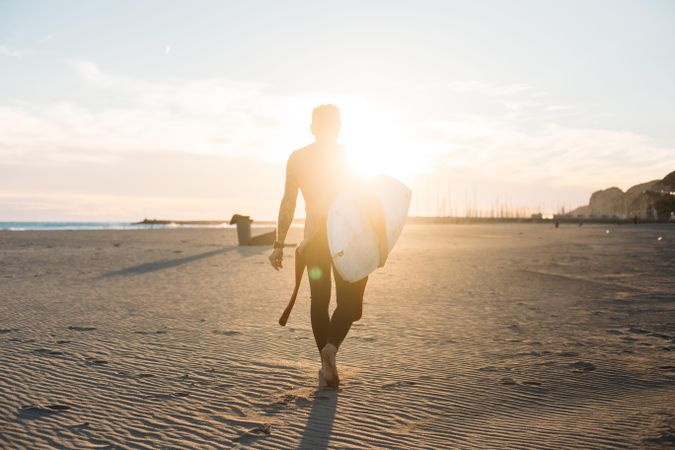 Man walking towards the sunset with surfboard