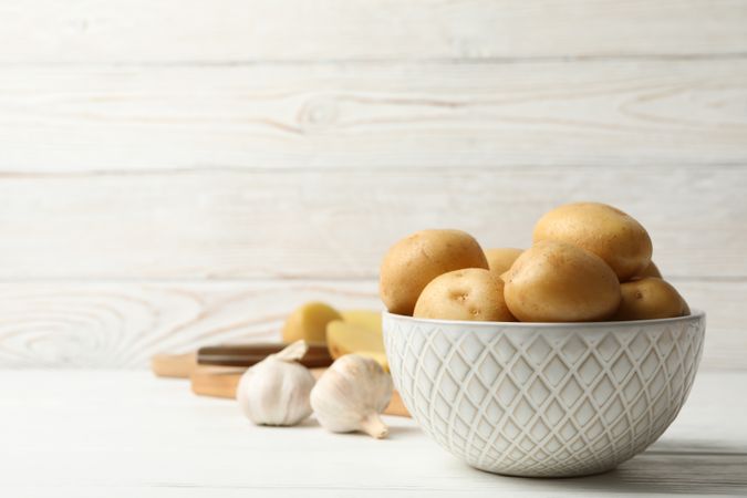 Side view of bowl full of potatoes on kitchen counter with garlic