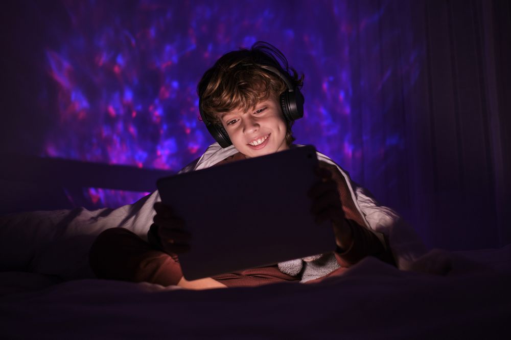 Positive boy in headphones watching video on tablet in darkness