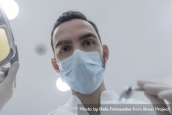 Low angle view of male dentist in medical mask holding dentist tools for dental procedure in clinic 5ky8Db