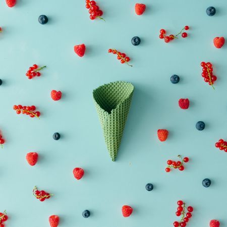 Green waffle cone on blue background with berries