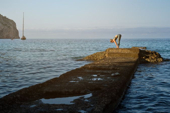 Woman practicing yoga on stone pier at sea