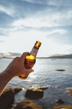 Bottle of beer in hand with seascape on background