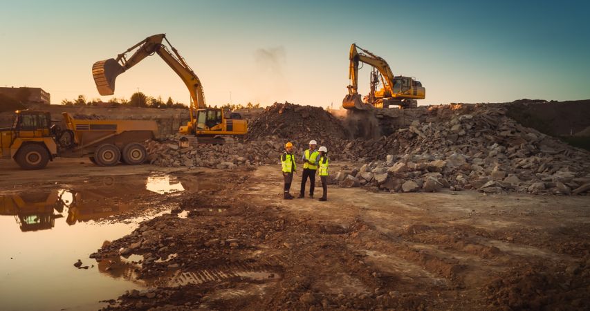 Aerial Drone Shot Of Construction Site With Heavy Machinery On Bright Sunny Day: Diverse Team of Real Estate Developers Discussing Project. Engineer, Architect, Urban Planner Talking And Using Tablet.