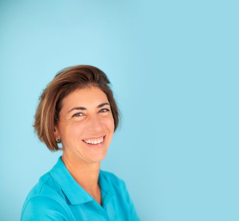 A woman, owner of her own physiotherapy clinic, smiles confidently, on a plain blue background