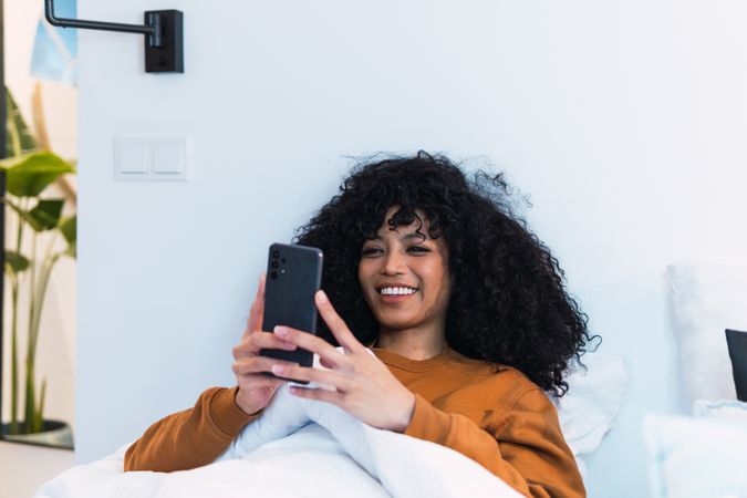 Happy Black woman using smartphone in bed