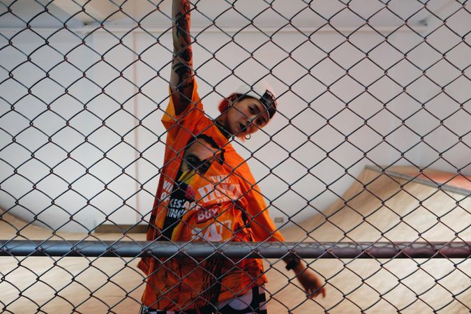 East Asian woman with dark lipsticks wearing orange shirt standing behind fence