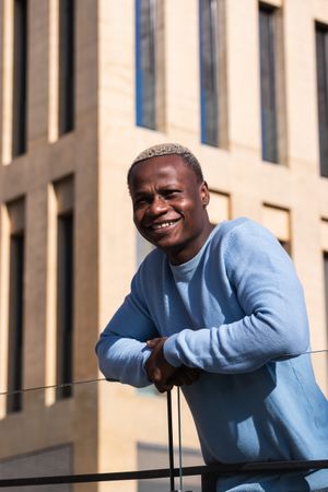 Happy Black guy resting on balcony of contemporary building