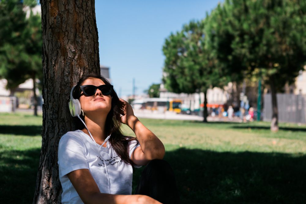 Relaxed trendy woman in headphones resting in park on grass