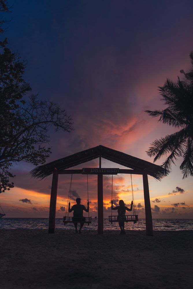 Silhouette of a man and a woman swinging at the beach during sunset